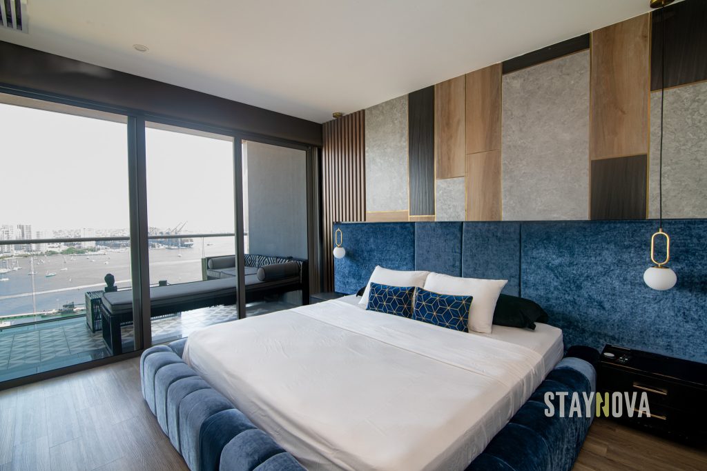 Habitación con cama doble, cabecera tapizada en azul y ventanales con vista a la ciudad, en una propiedad de alquiler turístico de Staynova en Colombia